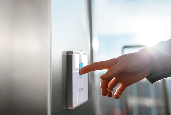 mano colocando dedo sobre lector de huella NÜO Awa de color blanco, para ingresar a una puerta controlada por un sistema de control de acceso